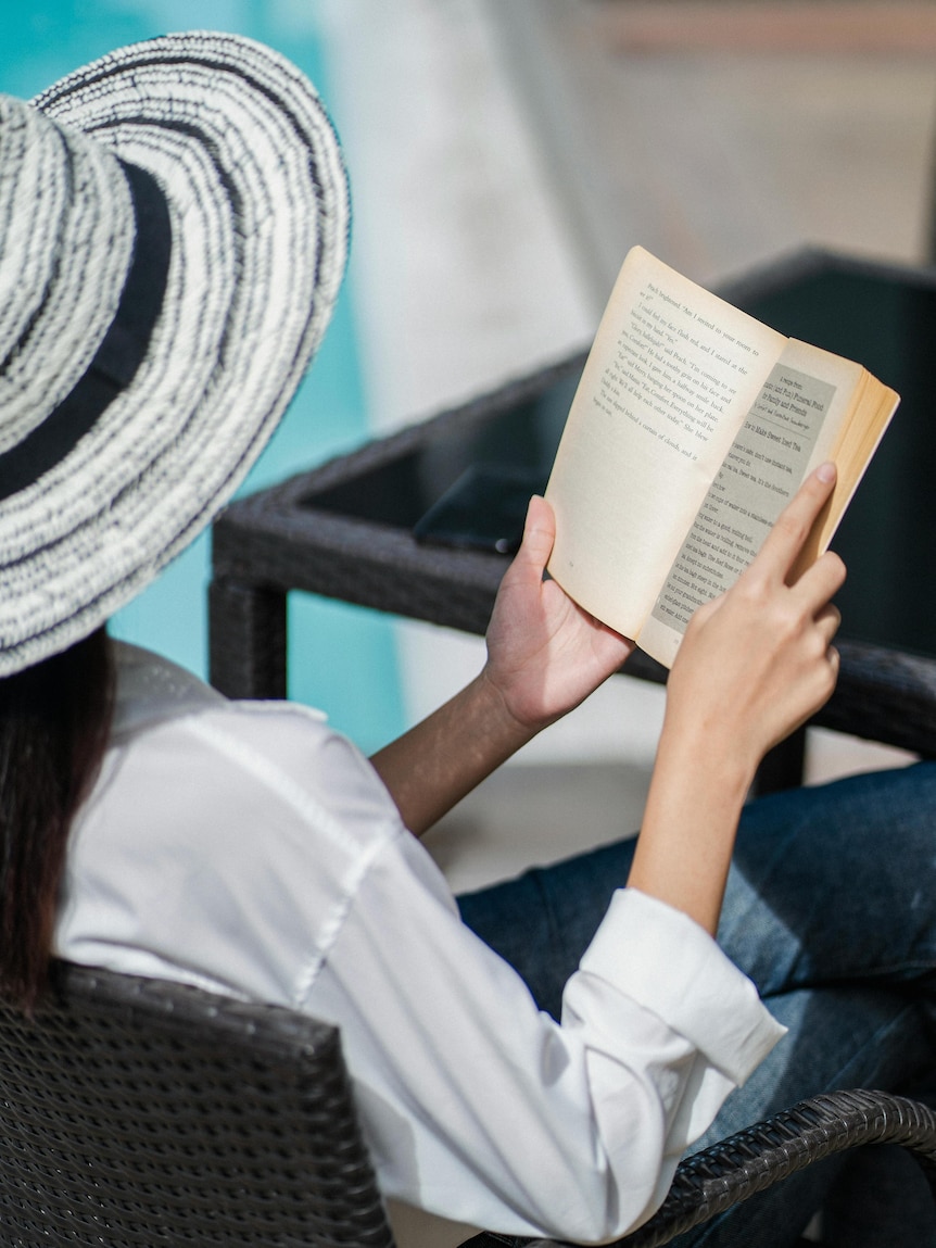 woman reads by the pool wearing a big hat