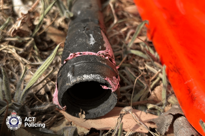 A metal pipe bomb post-detonation laying on grassy ground.