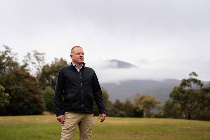 A man stands in a field with the mountain behind him