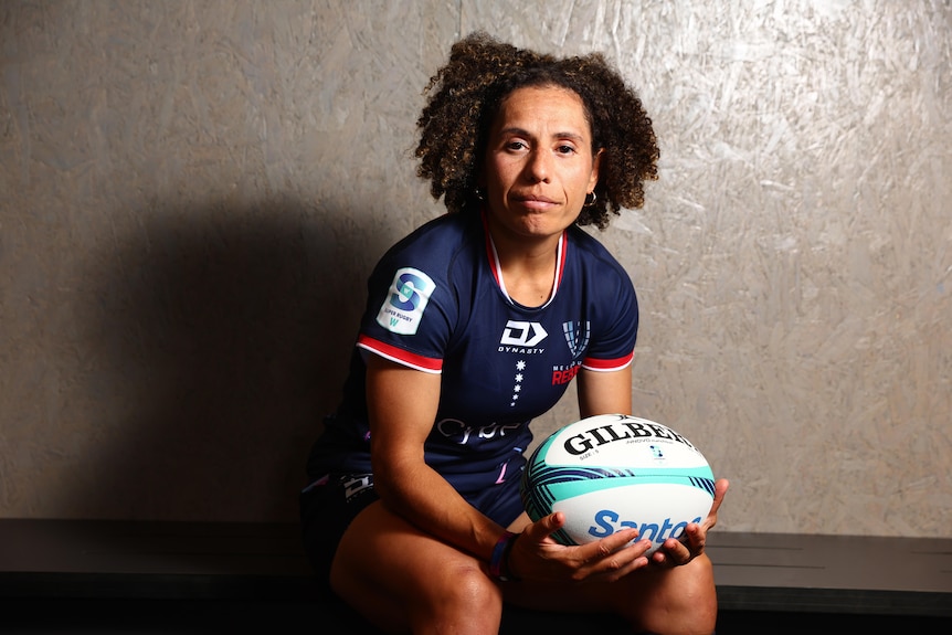 Melanie Kawa sits on a bench seat and holds a football.