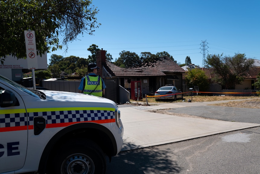 A wide shot of a roof caved in and a car at the front as police walk towards the house.