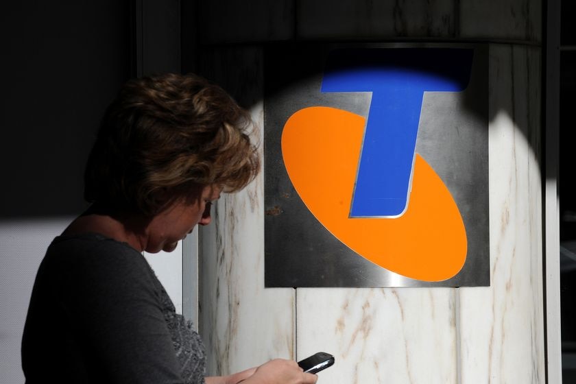 A woman checks her phone near a telstra sign.