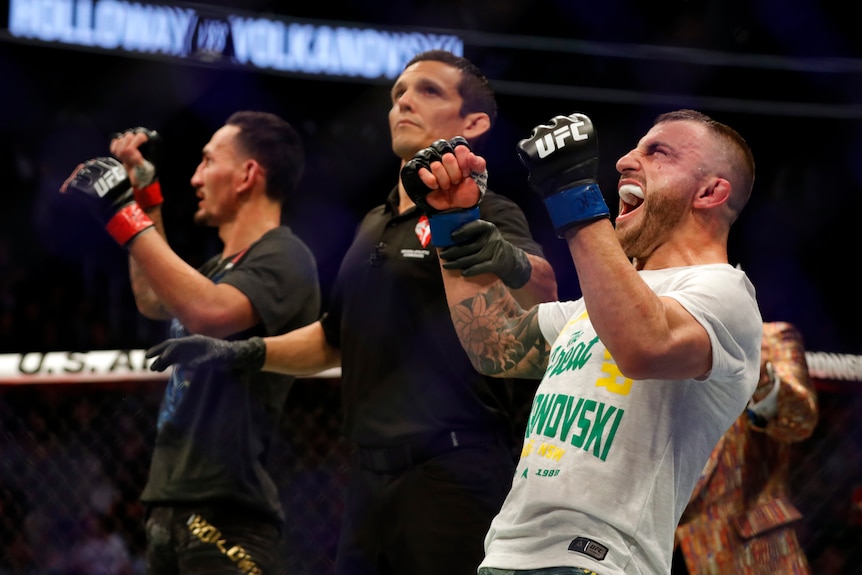 A man celebrates after winning a UFC title fight while the loser looks exasperated.