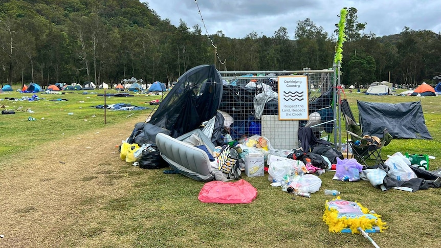 piles of rubbish bags and used camping gear piled up on a grassy festival ground