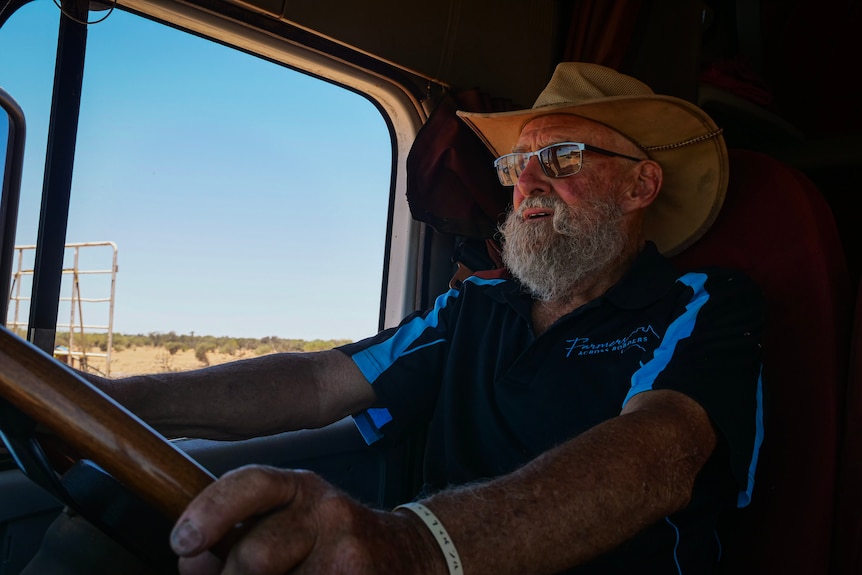 A man with a grey beard and glasses behind the wheel of a road train.