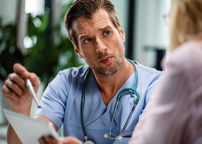 Male doctor in scrubs with stethoscope talking seriously to a patient, illustrating unprofessional things doctors have said.