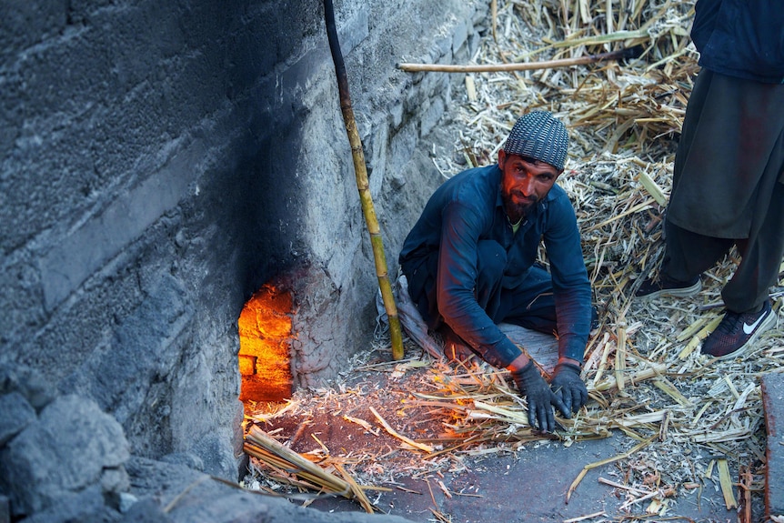 An Afghan man gathers kindling for a fire in a stone wall.