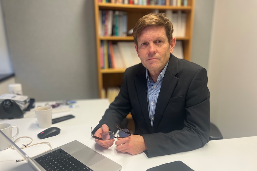 a man in a suit look at the camera from behind an office desk