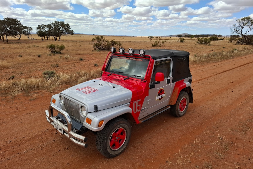 A red and grey jeep with Jurassic Park logo on its door on an outback road