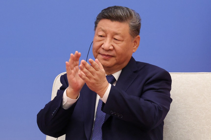 Xi Jinping applauds while sitting down in a dark blue suit.