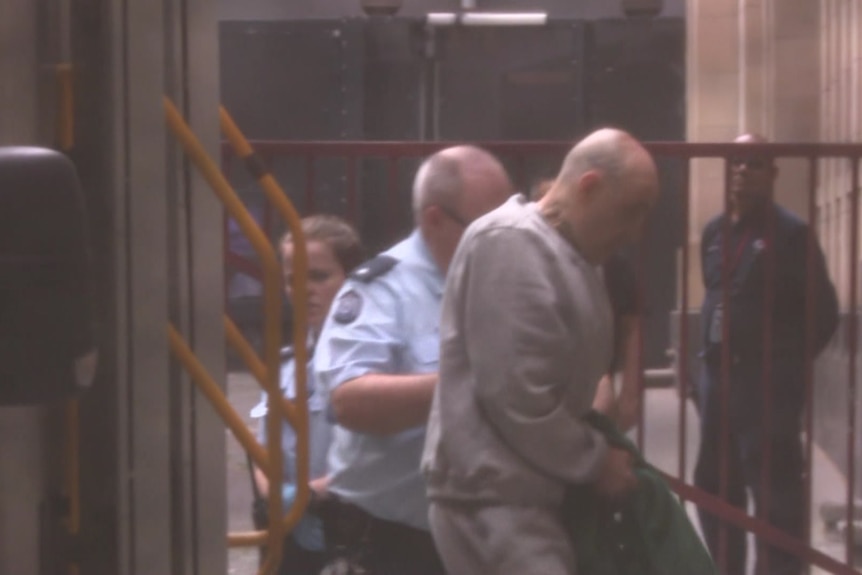 A man in a prison track suit exits a prison van inside the Supreme Court of Victoria