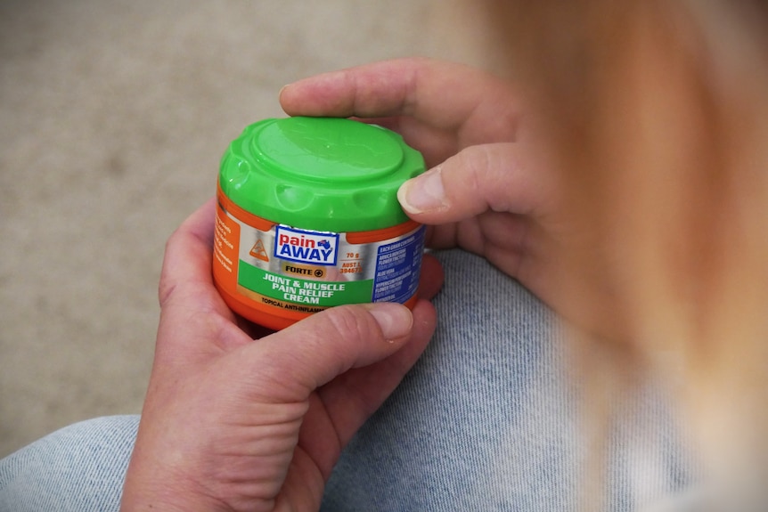 A container of topical pain relief cream in someone's hands.