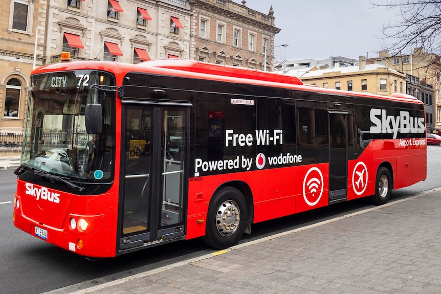 A large red bus in front of heritage brick buildings.