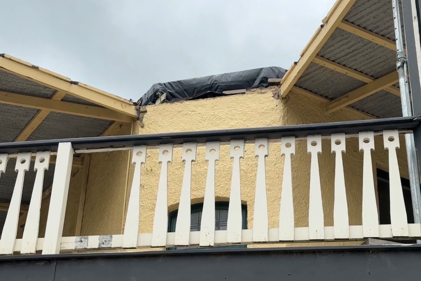 A photo of a yellow building, with a white fenced balcony and green pillars