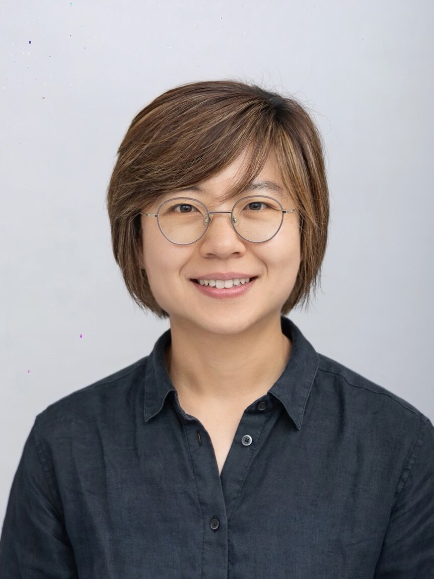 A professional headshot of a smiling young woman, Mirim Shin, wearing glasses and standing against a grey backdrop.