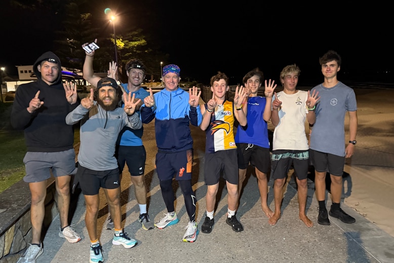 A group of eight people holding up fingers on a road at nighttime.