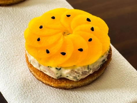 A round piece of food with a hard biscuit-like base and yellow circles of food with black seeds on top.