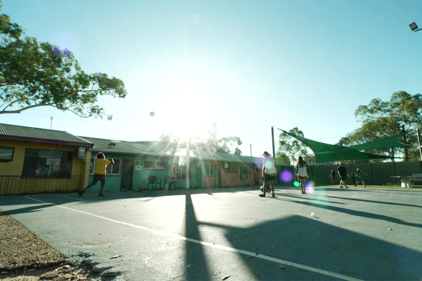 The sun shines over a basketball court as children play