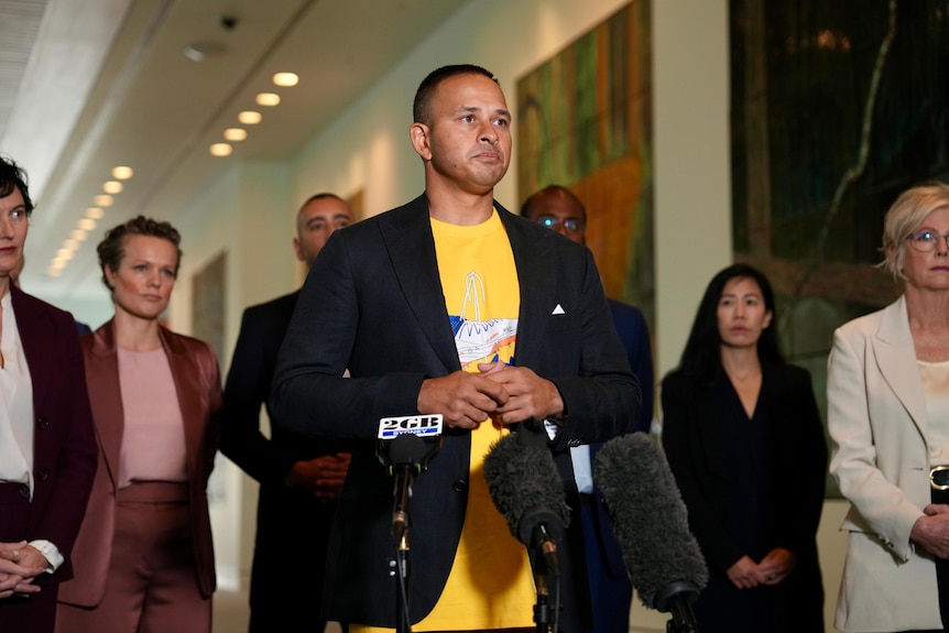 A man wearing a yellow shirt speaks to the media.