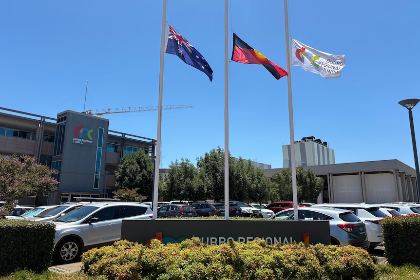Australian, Indigenous, and Dubbo Regional Council flags fly at half mast in front of a council building.
