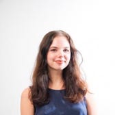 girl with brown hair and blue shirt smiling in front of plain white background