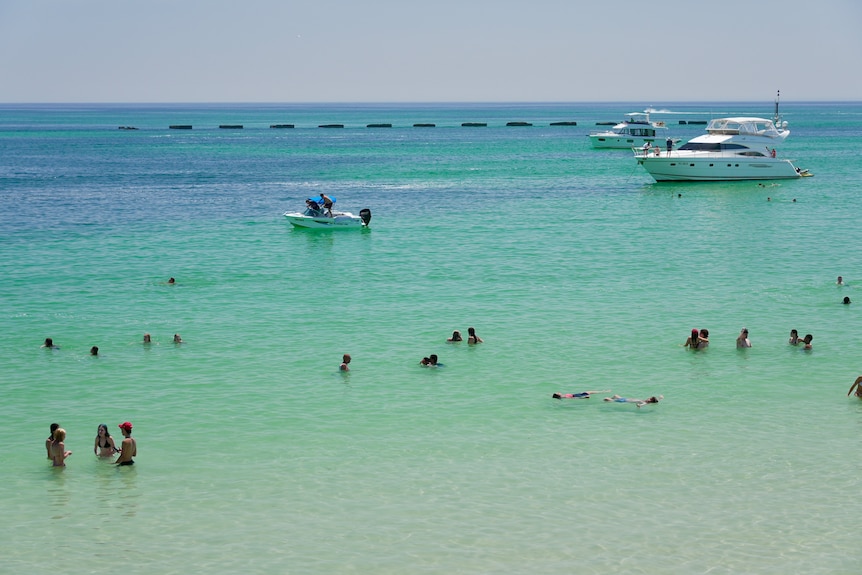 Swimmers and boats in sea waters at Glenelg on a sunny day.