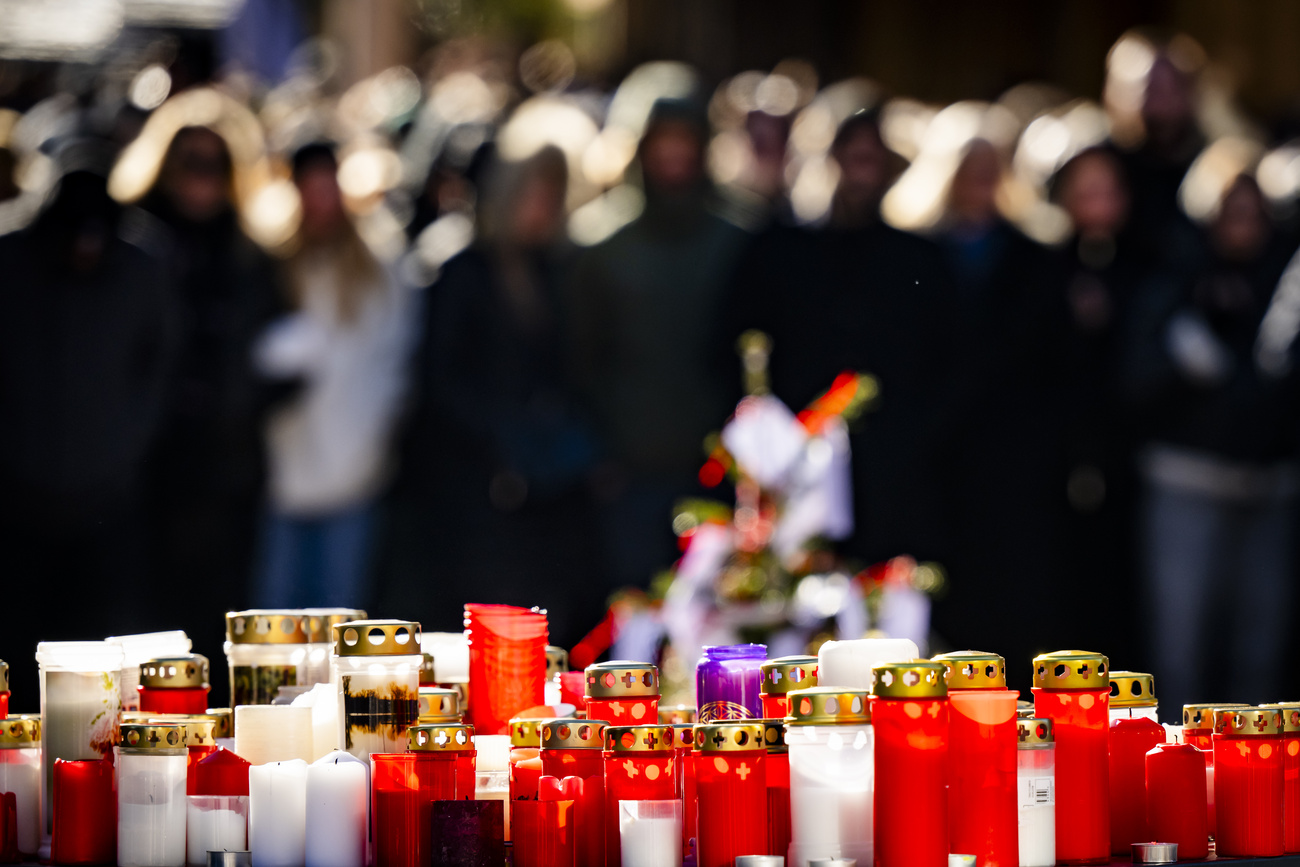 Mourners gather around flowers and candles to commemorate the victims of the fire at the "Le Constellation" bar and lounge, in Crans-Montana, Switzerland, on Sunday, January 4, 2026. 40 persons lost their lives and over 100 were severely injured in the fire at the bar "Le Constellation" on New Year's Eve in the Swiss Alps resort of Crans-Montana. (KEYSTONE/Jean-Christophe Bott)
