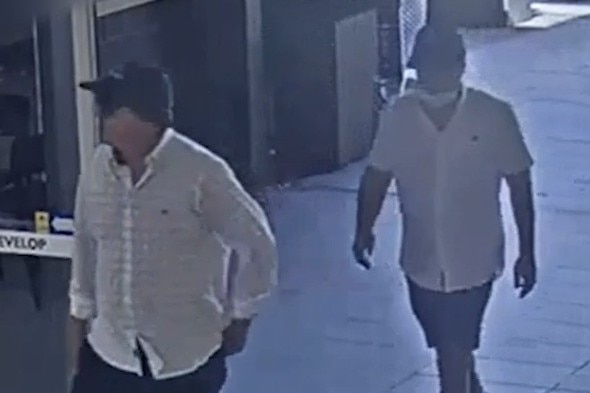 Two men in white shirts and dark caps walk through an automatic door.