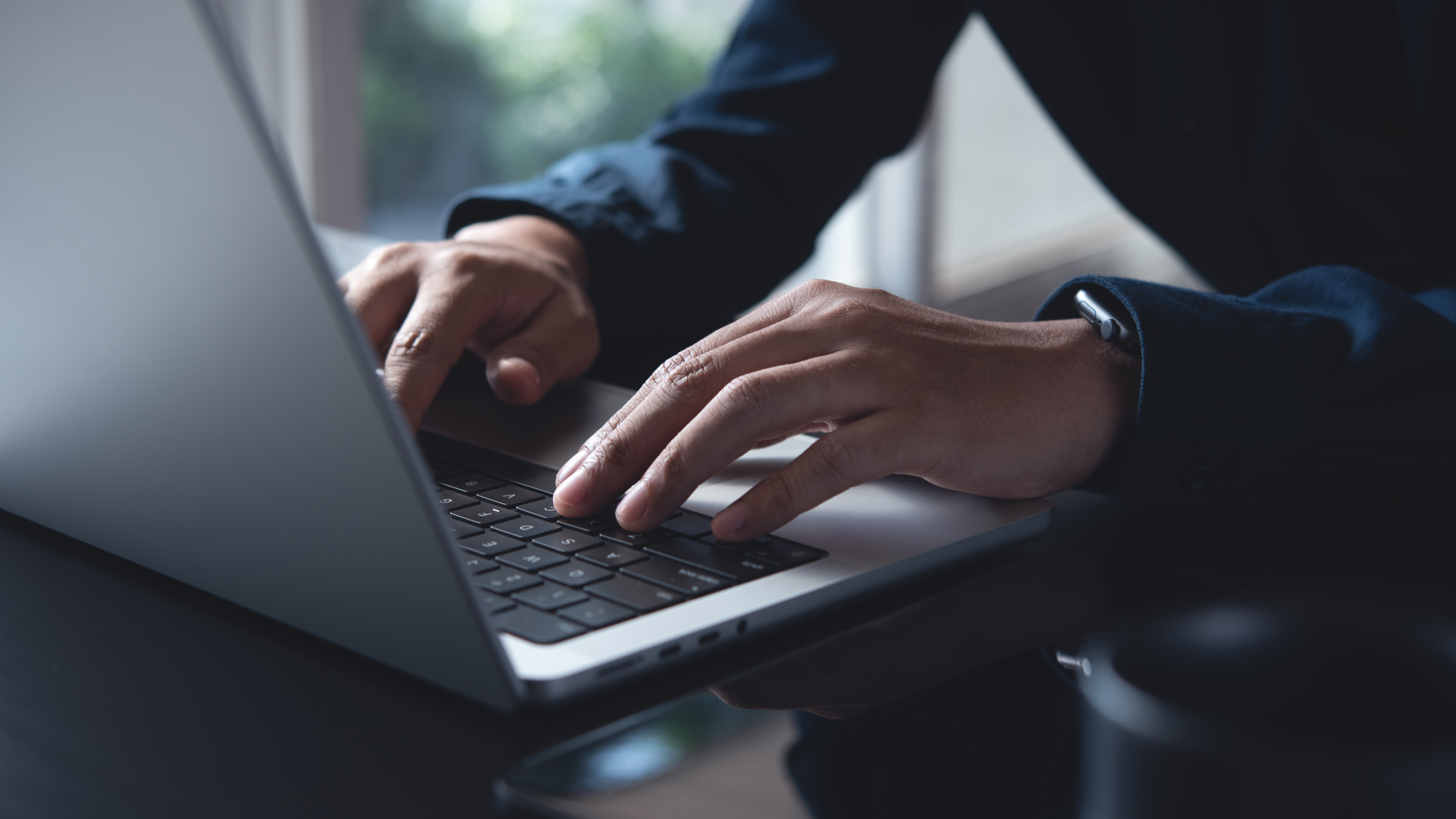 A close up photo of someone's hands while typing on a laptop