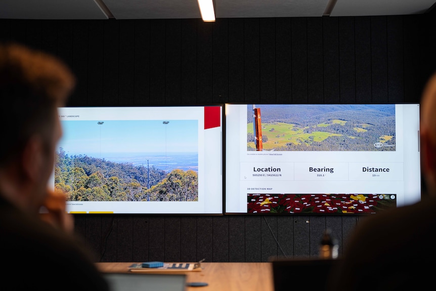 Two men sitting at a desk with computers looking at screens