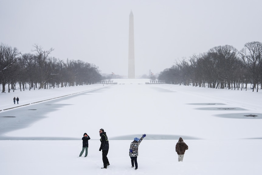 People play in the snow with the Washington monument in the background and a frozen Lincoln Memorial Remembrance pool.