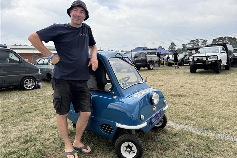 A man stands next to a vintage microcar.