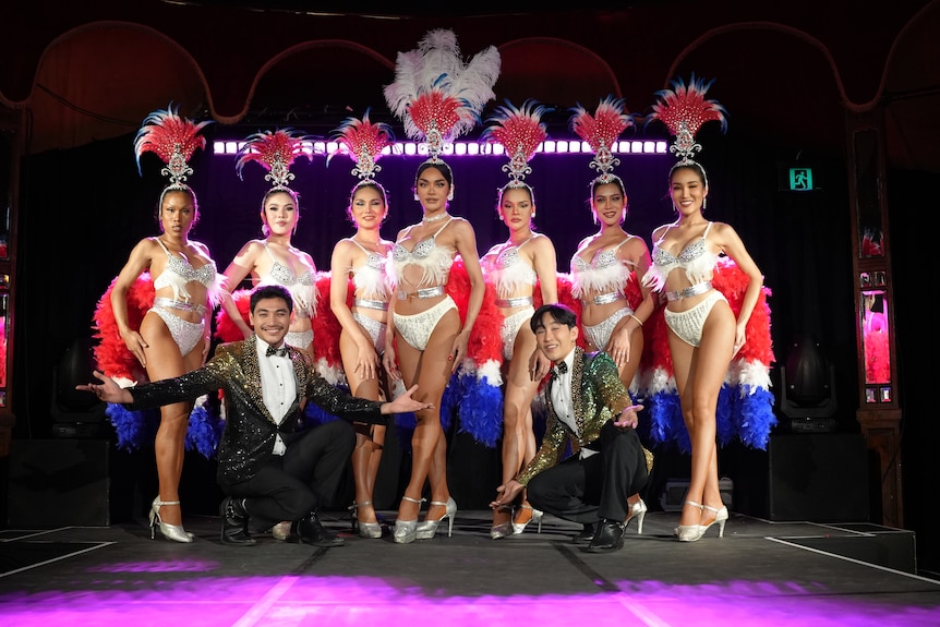 A line of Thai cabaret dancers as two male performers kneel at their feet