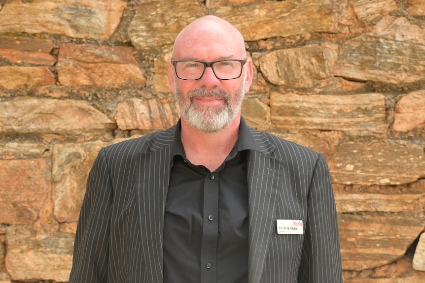 A bald man in a dark suit smiles