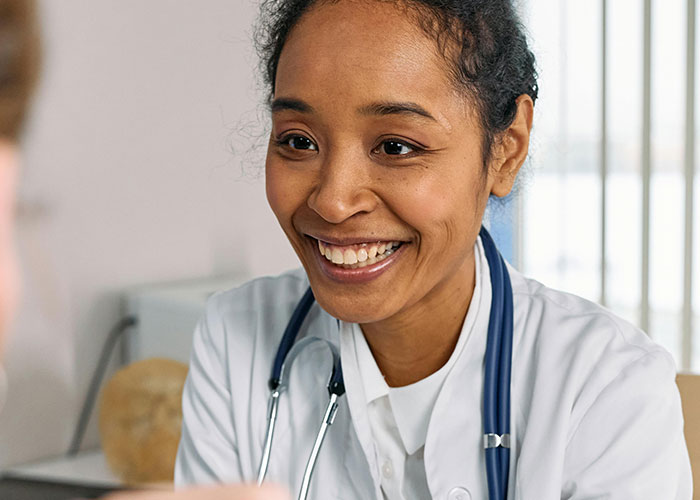 Smiling medical professional with stethoscope listening and engaging warmly with a patient during a consultation.