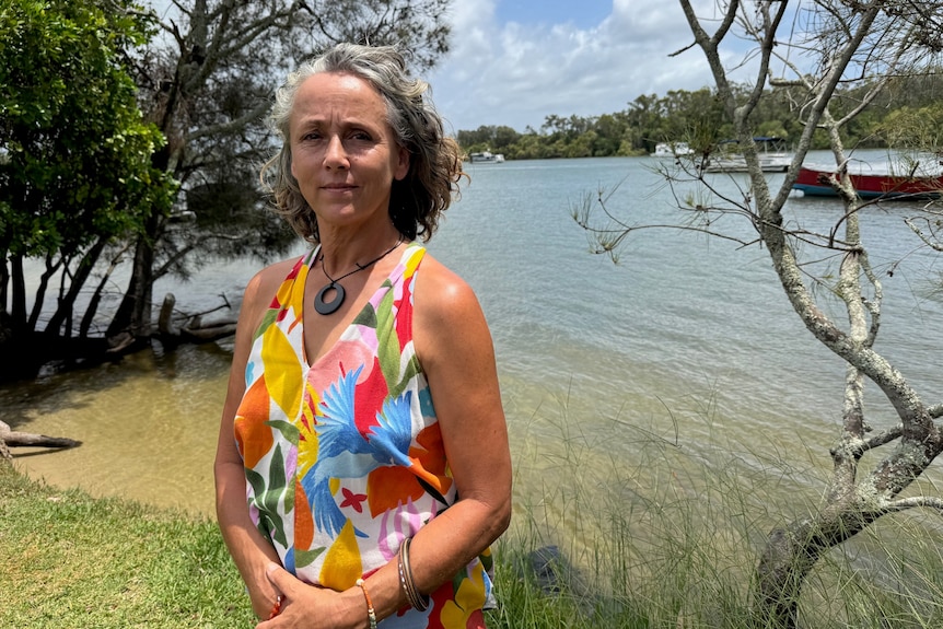 Woman in bright dress by water's edge with houseboats in background.