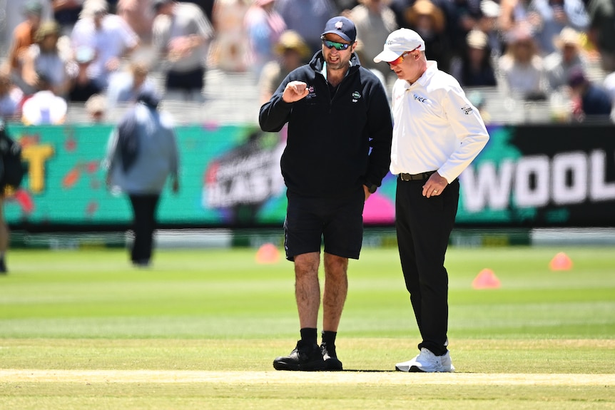 A curator talks to an official as they look at the pitch during a break in a cricket Test at the MCG.