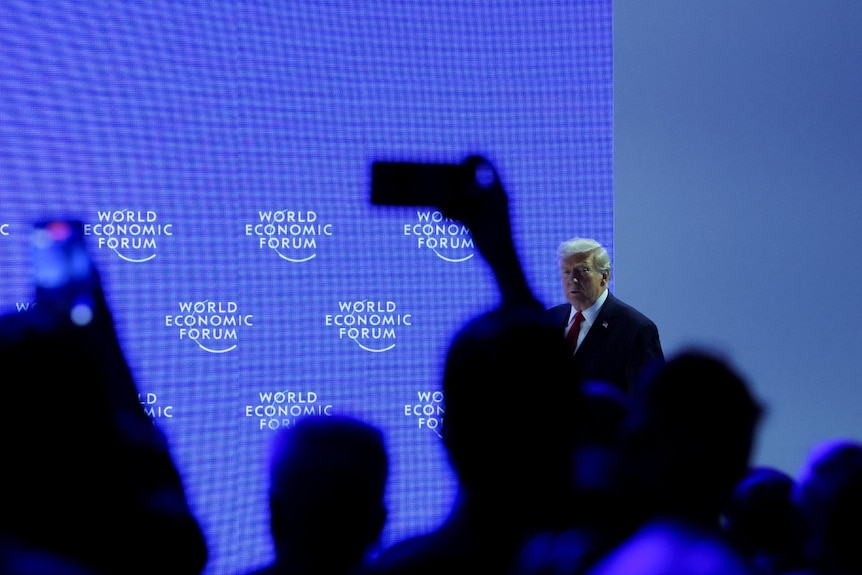 A man in a suit walking, seen from behind a large crowd.