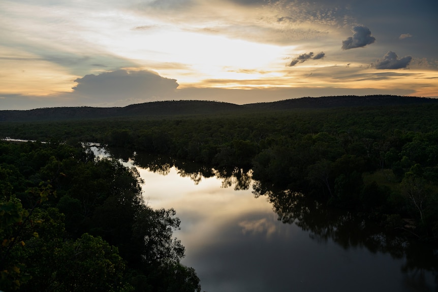 An image of a silhouetted bushland along banks of winding river at sunset 