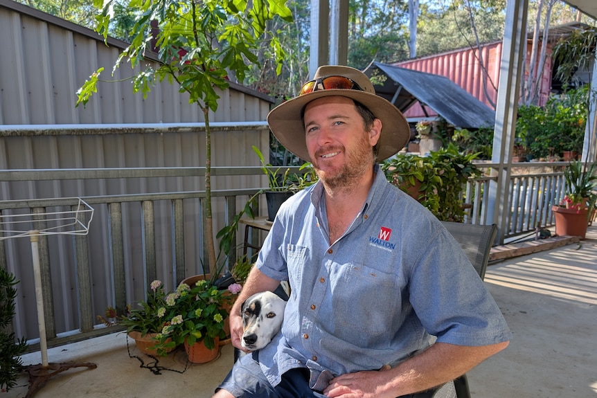 Phil Walton wears a hat and sits next to a dog on a verandah as he looks at the camera.