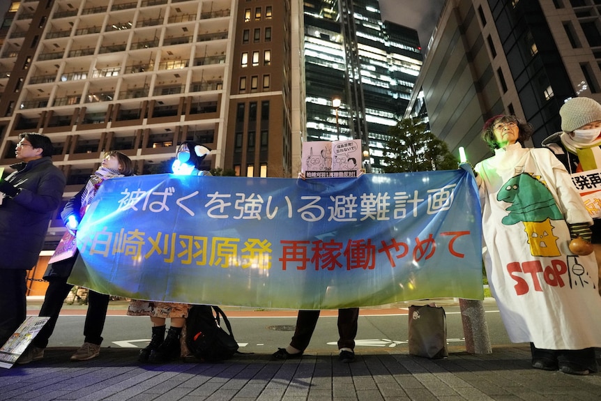 Protesters hold a long, colourful banner expressing concerns about a nuclear power plant restarting