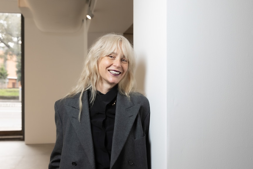 Woman with blonde hair and in grey blazer smiles at camera 