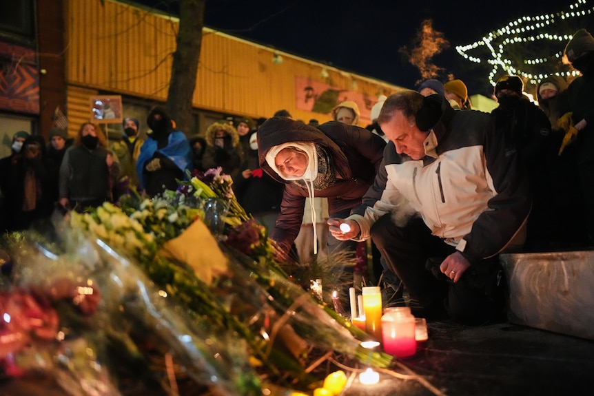 Members of the public leaving flowers and candles at a make-shift memorial at night.