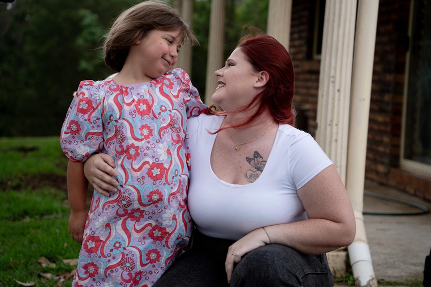 Little girl in pink dress hugging woman with red hair in white top