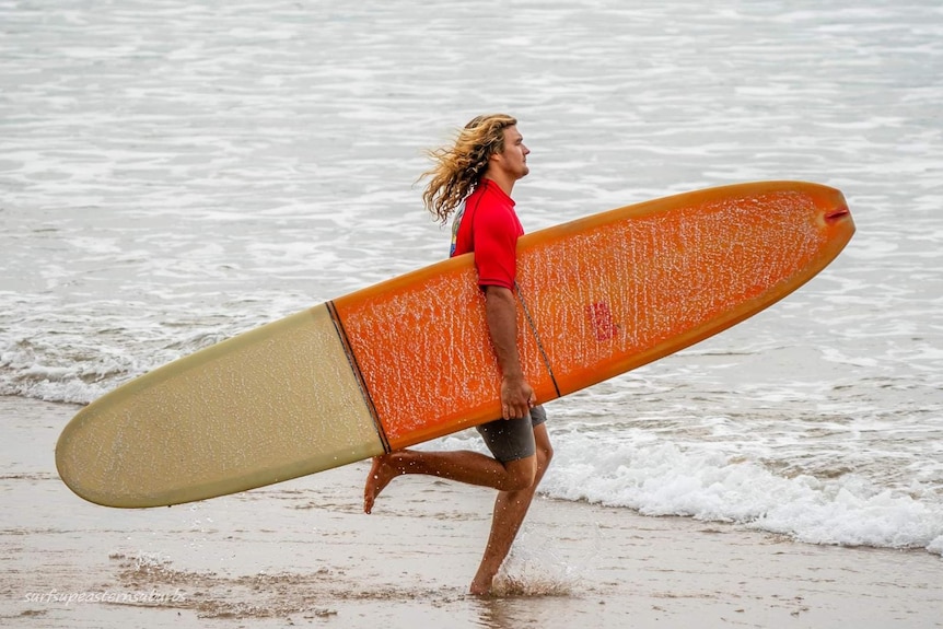 A man running into the water with an orange surfboard
