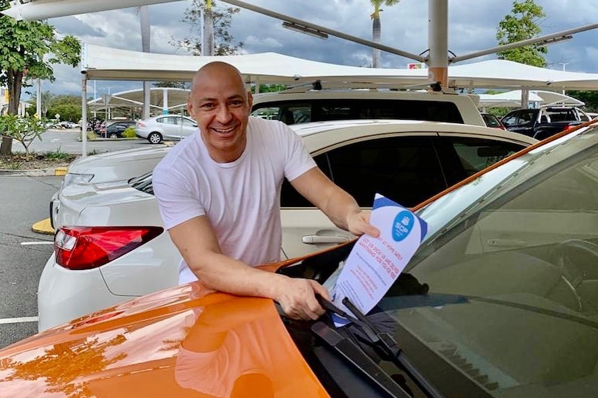 A man places a piece of paper under a car's windscreen wipers.