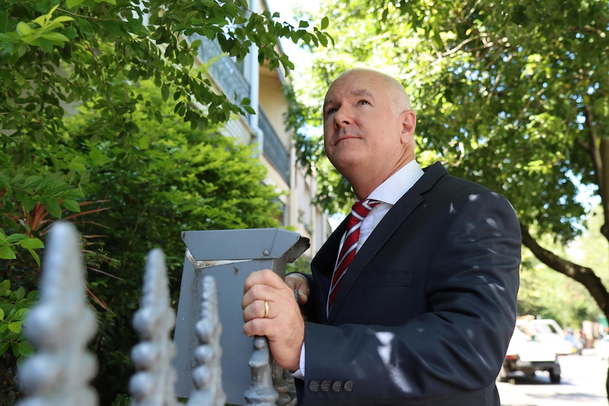 A man in a suit and tie is pictured on a leafy street.