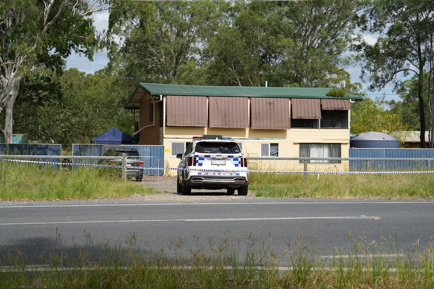A police car in the driveway of a house with a road and grass in the foreground.