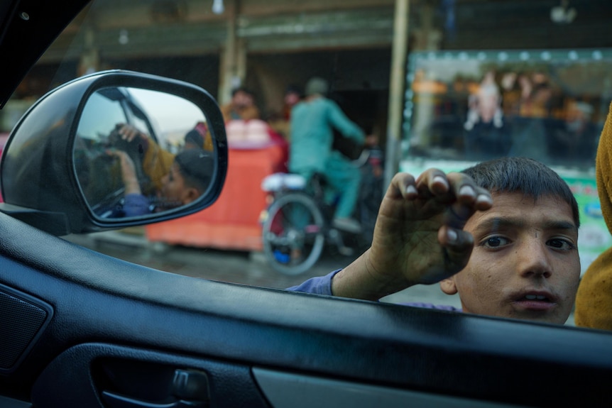 An Afghan boy holds his hand against a car window.