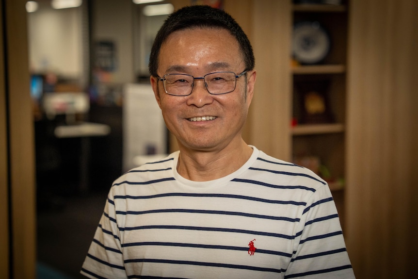 a man smiles at the camera wearing a striped top and glasses.